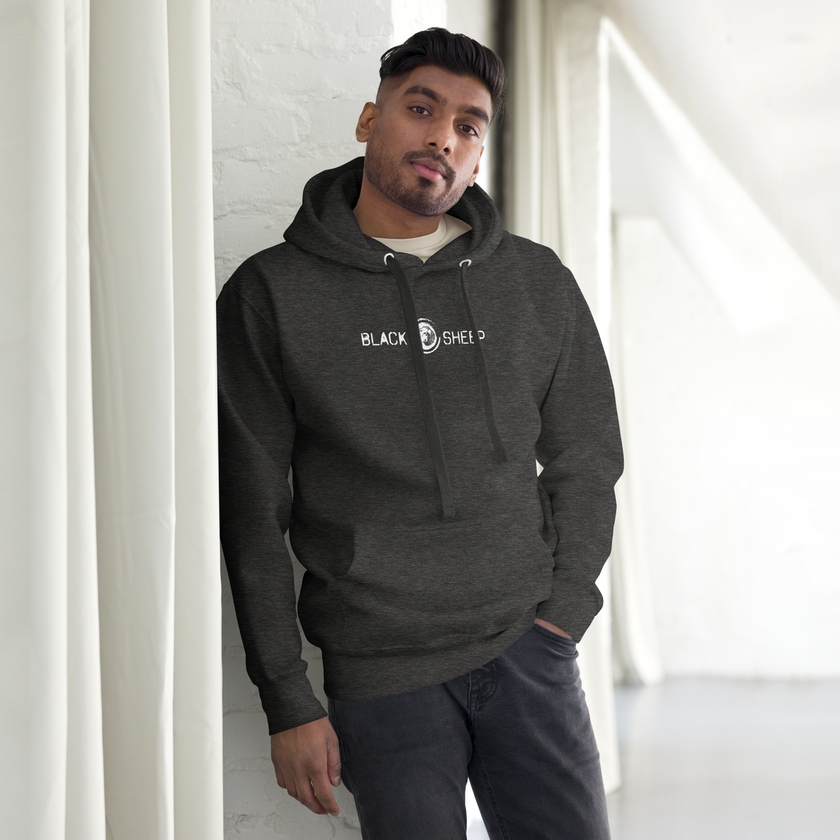 Mann trägt grauen Unisex Hoodie mit Black Sheep Schriftzug und kleinem Schafskopf auf Brusthöhe