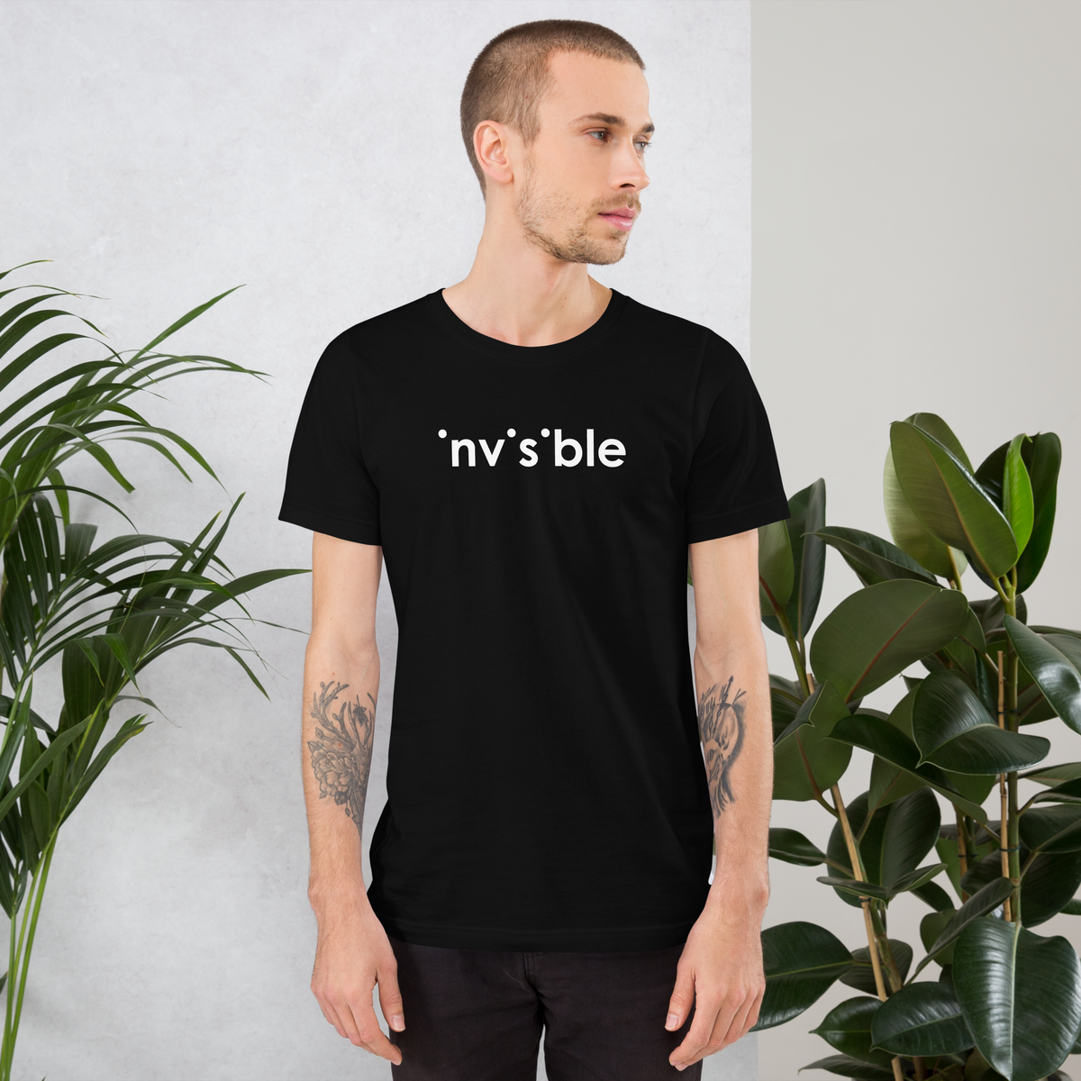 Mann trägt schwarzes Unisex T-Shirt mit weißem Invisible Schriftzug, bei dem die i-Punkte fehlen Brustprint