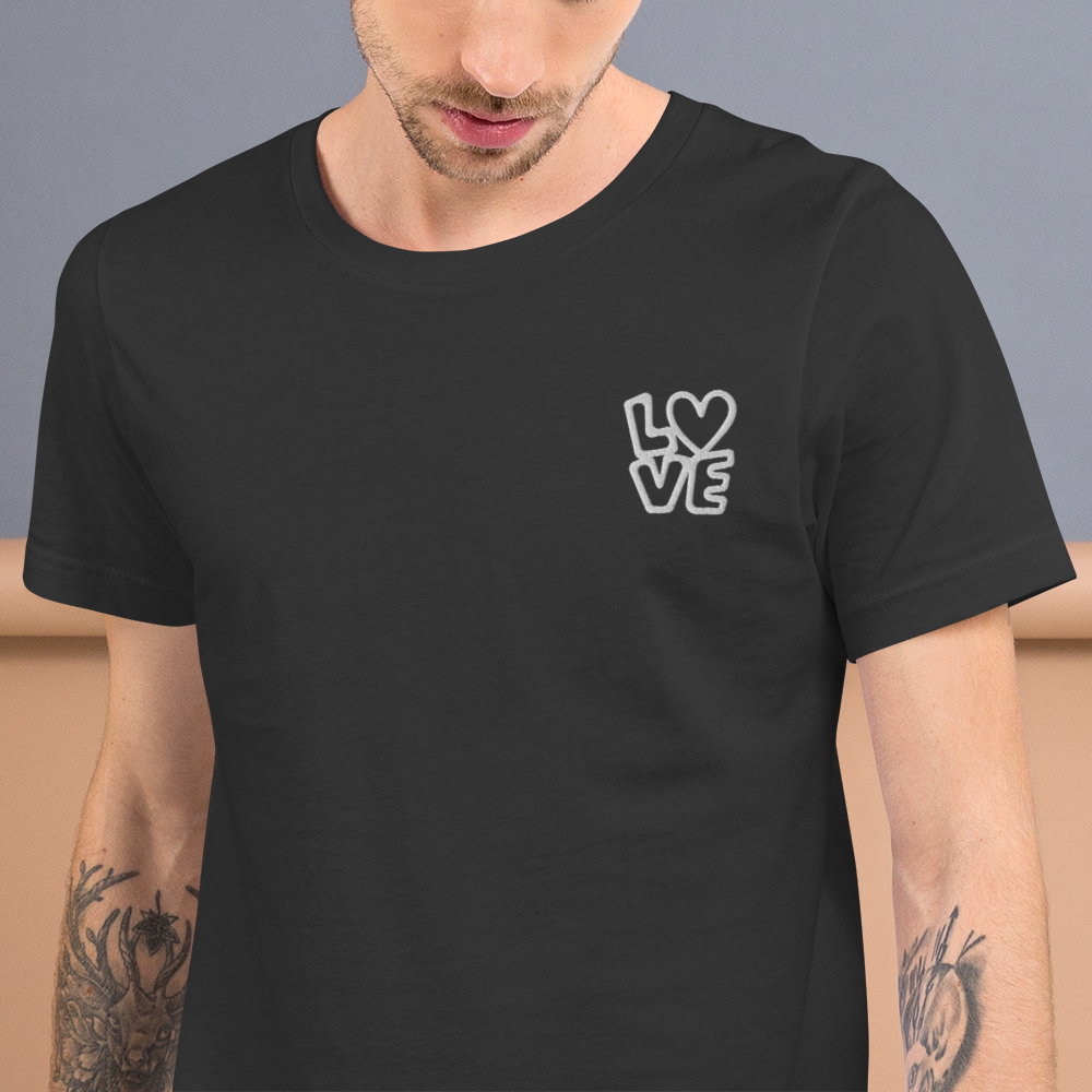 Mann trägt graues Unisex T-Shirt mit LOVE Stickerei bei dem das O durch ein Herz ersetzt ist