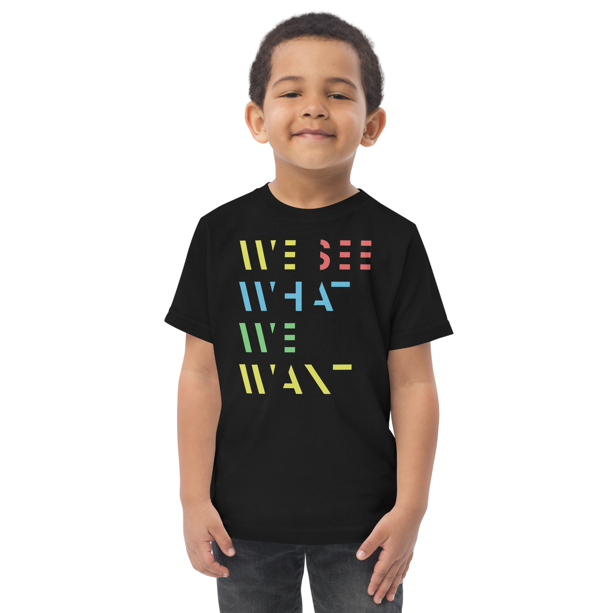 Junge trägt schwarzes T-Shirt mit buntem We See What We Want Schriftzug