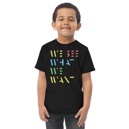 Junge trägt schwarzes T-Shirt mit buntem We See What We Want Schriftzug